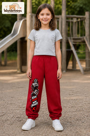 Mädchen trägt rote Jogginghose mit Risk More Würfel-Print, von vorn auf dem Spielplatz.