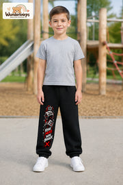 Junge trägt schwarze Jogginghose mit Risk More Würfel-Print, von vorn auf dem Spielplatz.
