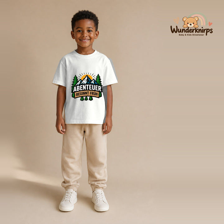 T-Shirt für Jungen in Weiß mit Motiv „Abenteuer beginnt früh“, getragen von einem Kind – Wunderknirps.