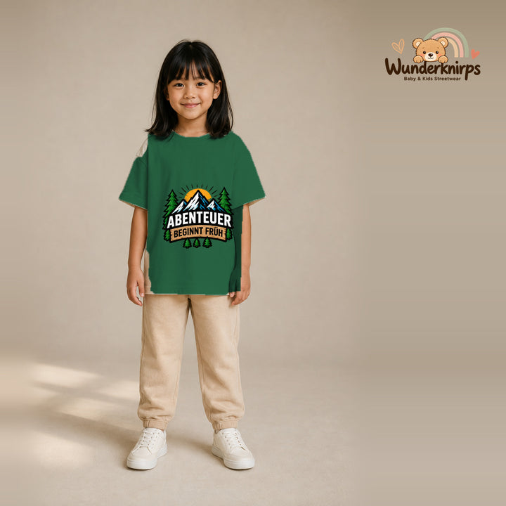 T-Shirt für Mädchen in Grün mit Motiv „Abenteuer beginnt früh“, getragen von einem Kind – Wunderknirps.