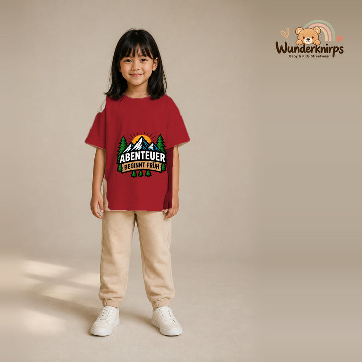 T-Shirt für Mädchen in Rot mit Motiv „Abenteuer beginnt früh“, getragen von einem Kind – Wunderknirps.