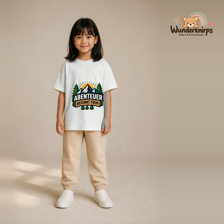 T-Shirt für Mädchen in Weiß mit Motiv „Abenteuer beginnt früh“, getragen von einem Kind – Wunderknirps.