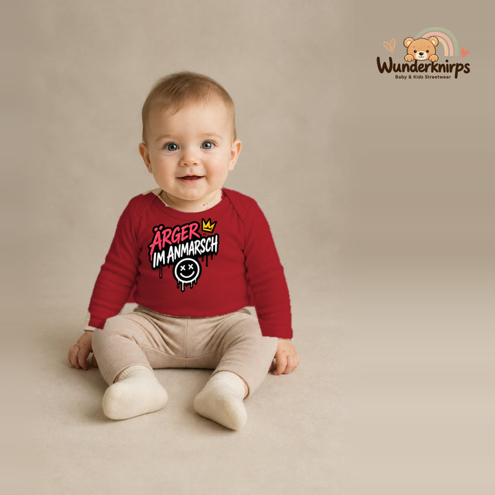 Babybody für Jungen in Rot mit Motiv „Ärger im Anmarsch“, getragen von einem Kind – Wunderknirps.