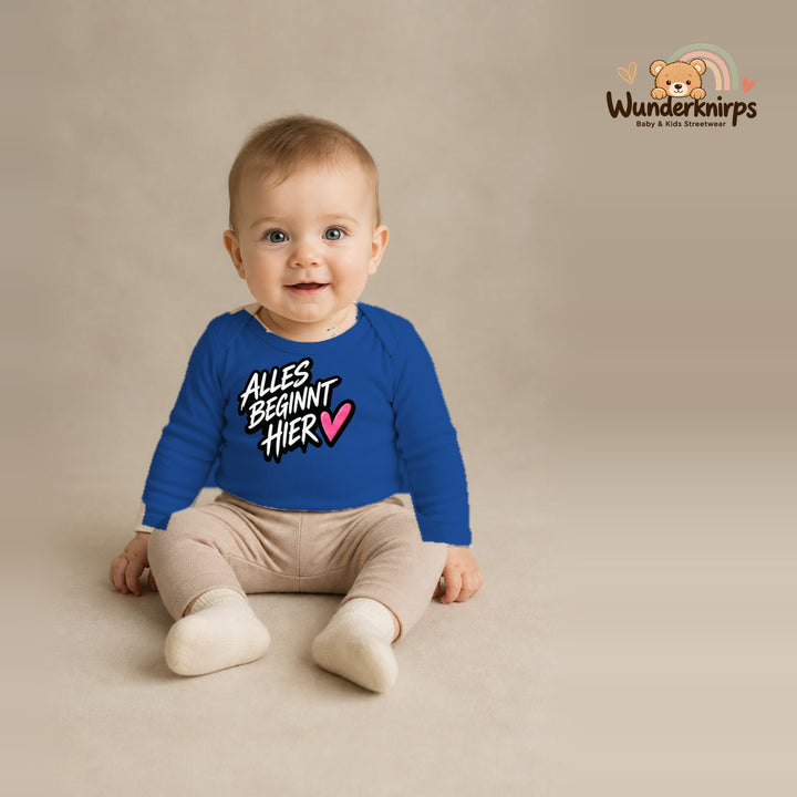 Babybody für Jungen in Blau mit Motiv „Alles beginnt hier“, getragen von einem Kind – Wunderknirps.