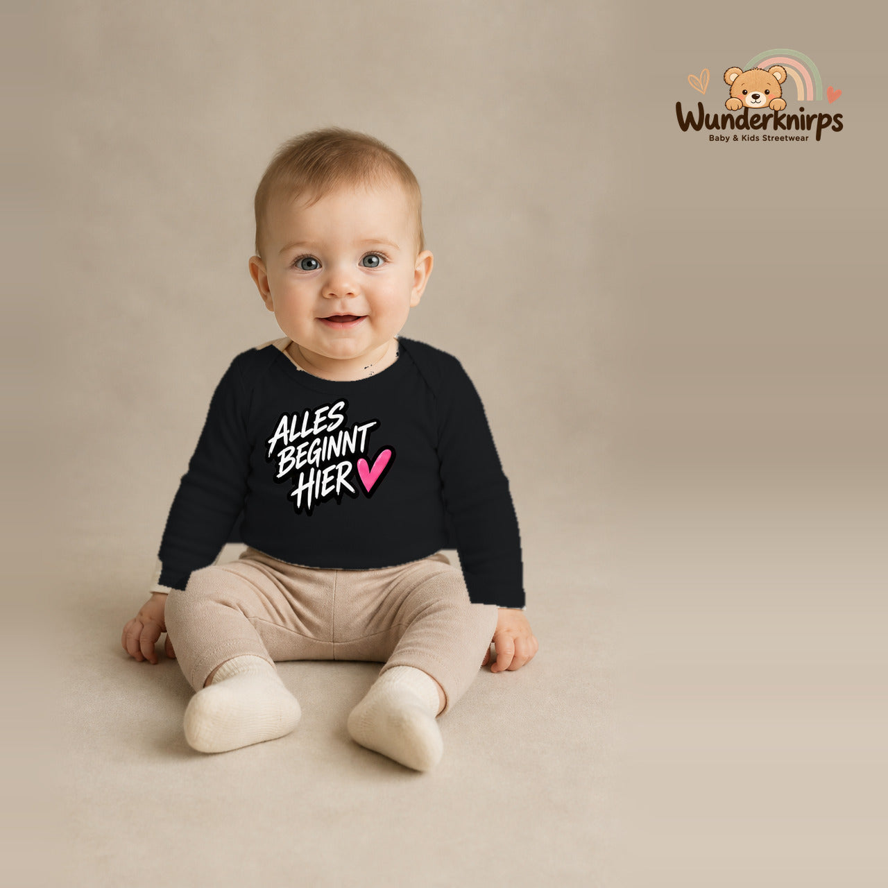 Babybody für Jungen in Schwarz mit Motiv „Alles beginnt hier“, getragen von einem Kind – Wunderknirps.