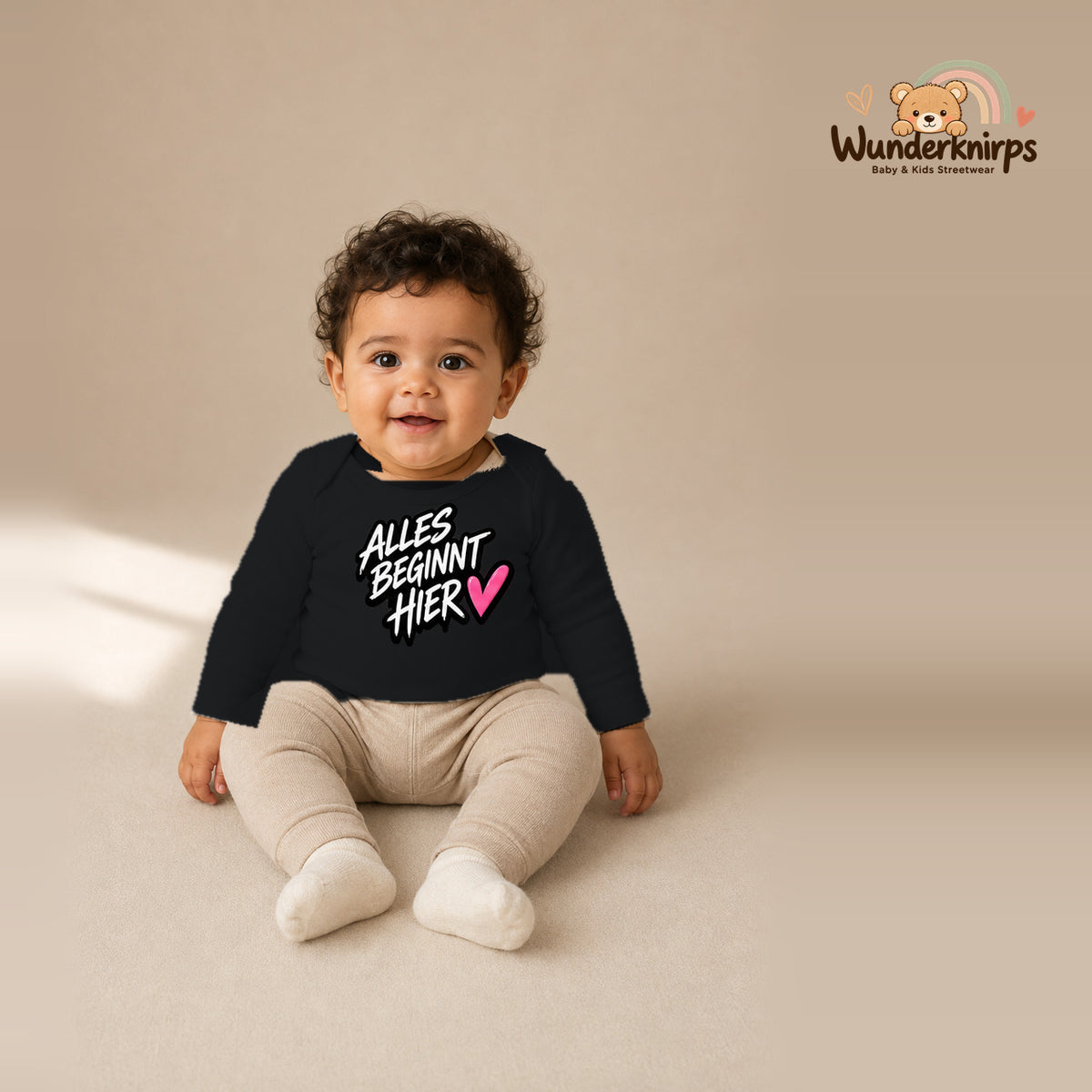 Babybody für Jungen in Schwarz mit Motiv „Alles beginnt hier“, getragen von einem Kind – Wunderknirps.
