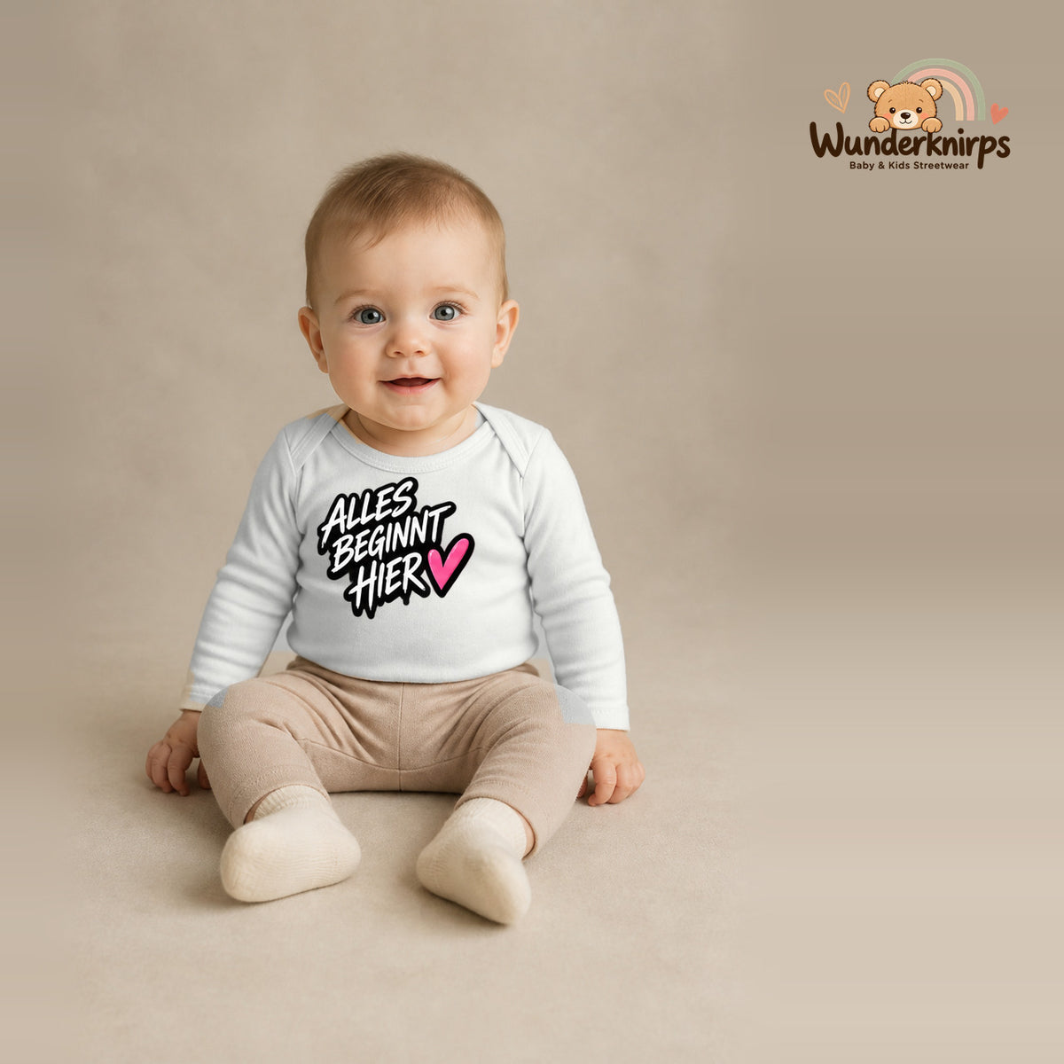 Babybody für Jungen in Weiß mit Motiv „Alles beginnt hier“, getragen von einem Kind – Wunderknirps.