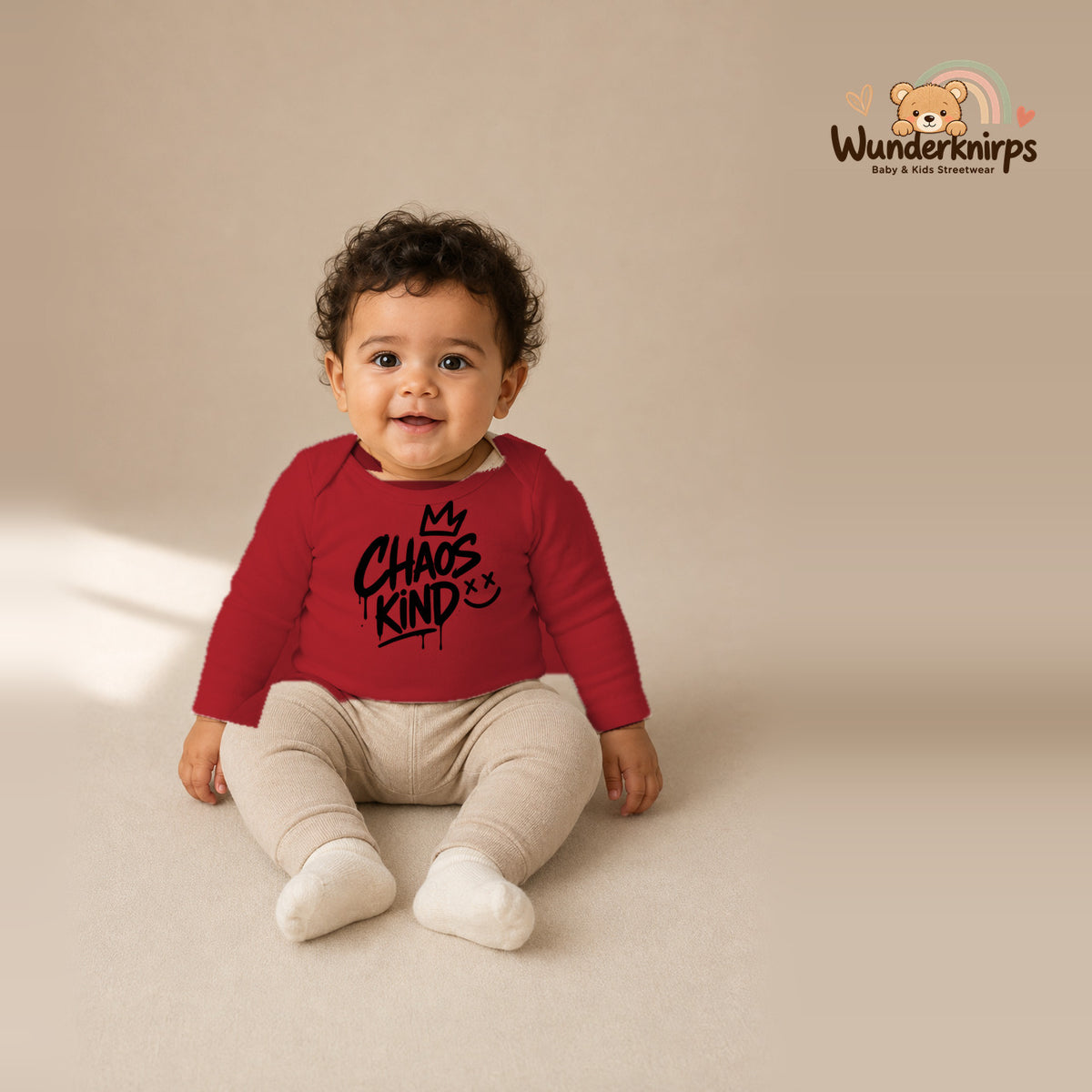 Babybody für Jungen in Rot mit Motiv „Chaoskind“, getragen von einem Kind – Wunderknirps.