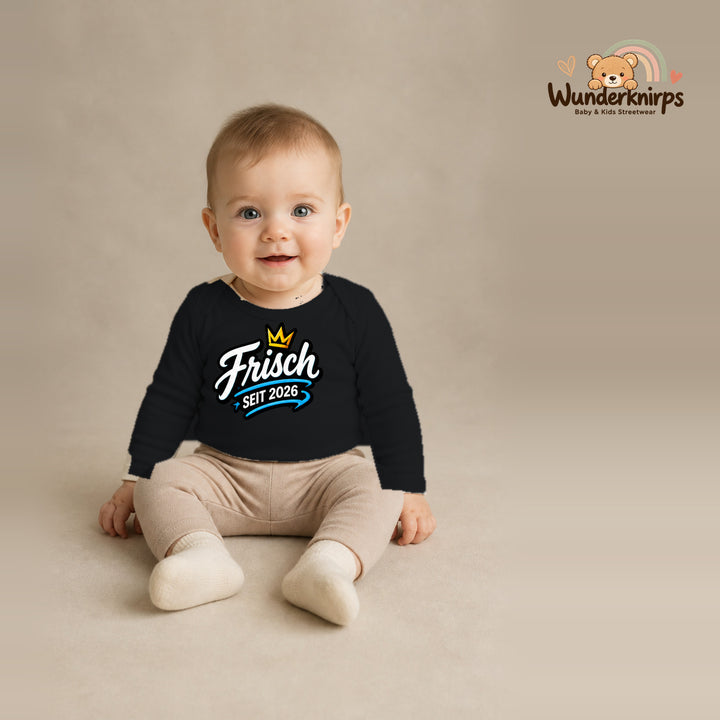 Babybody für Jungen in Schwarz mit Motiv „Frisch seit 2026“, getragen von einem Kind – Wunderknirps.