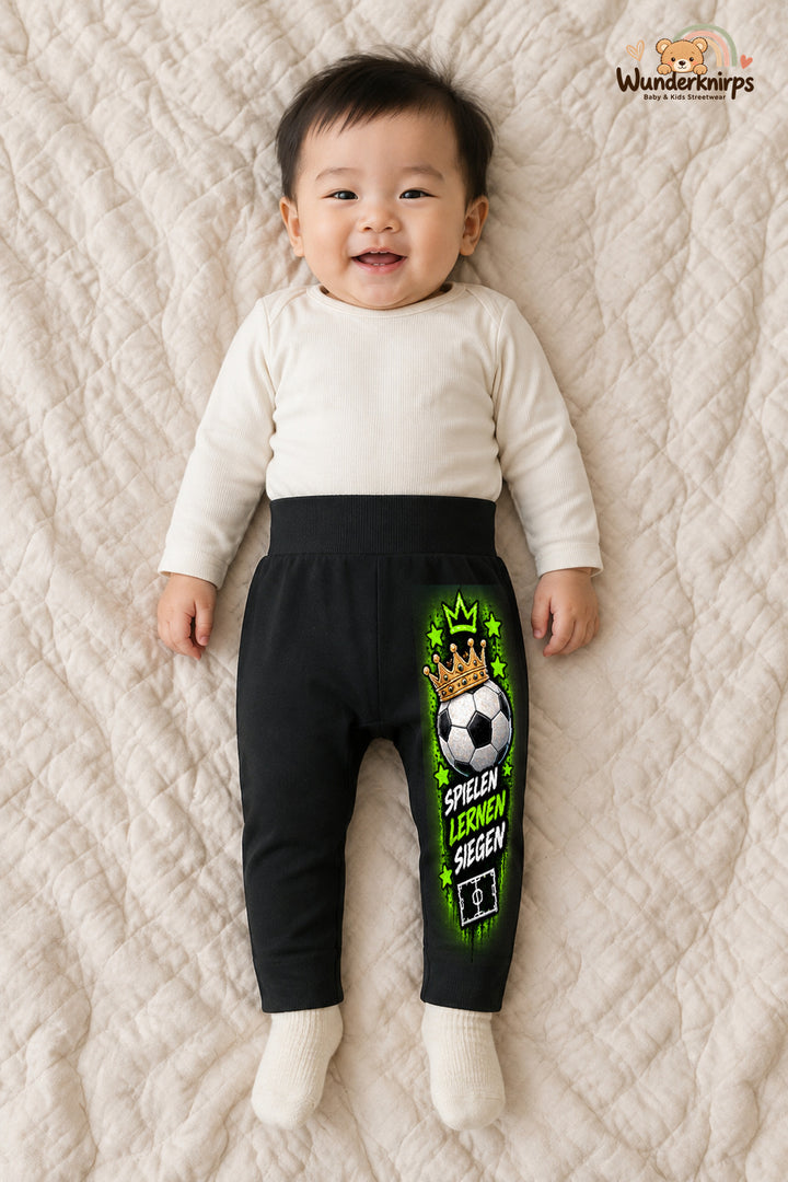 Fußball Alltagsheld – Spielen lernen siegen – Babyhose für Jungen: Schwarz mit Fußball-Druck am Hosenbein – Wunderknirps.