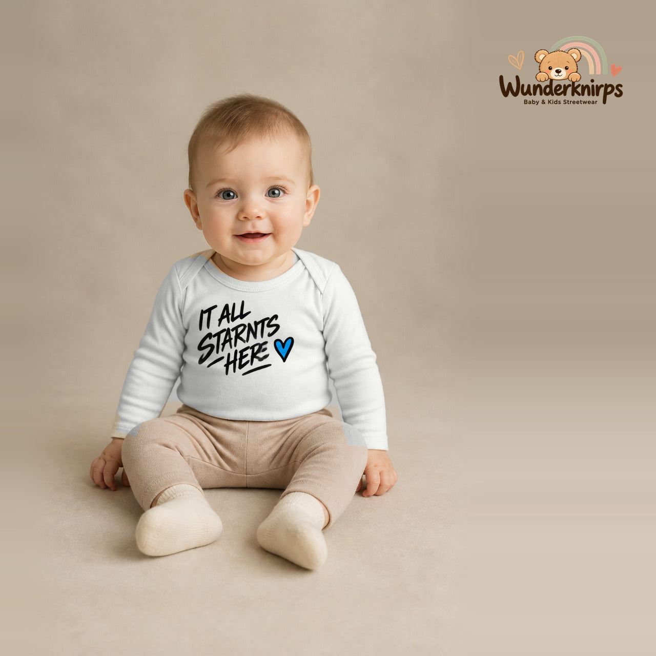 Babybody für Jungen in Weiß mit Motiv „It all starts here“, getragen von einem Kind – Wunderknirps.