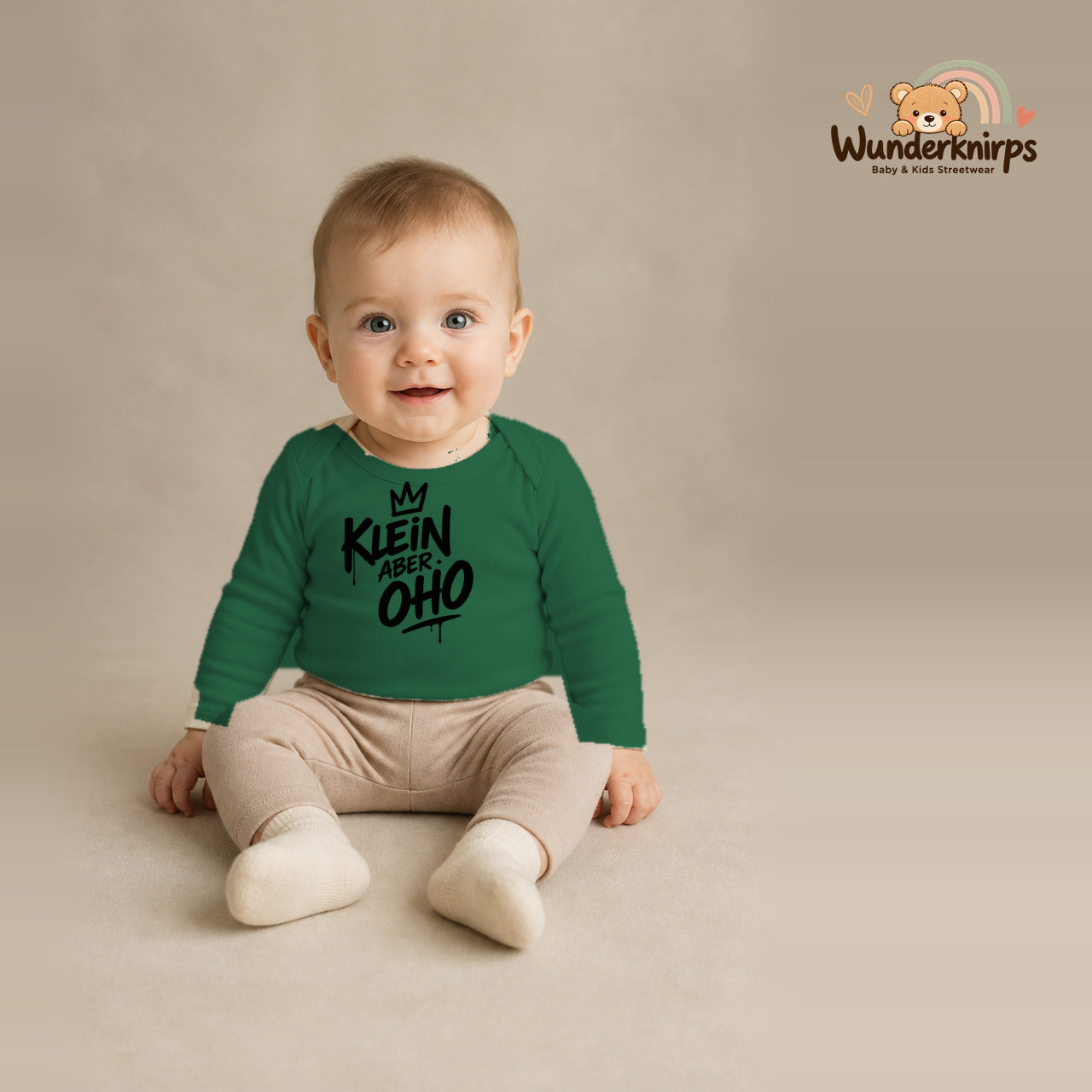 Babybody für Jungen in Grün mit Motiv „Klein aber oho“, getragen von einem Kind – Wunderknirps.