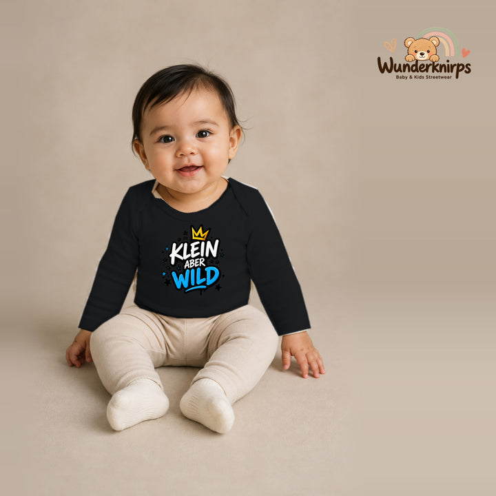 Babybody für Mädchen in Schwarz mit Motiv „Klein aber wild“, getragen von einem Kind – Wunderknirps.