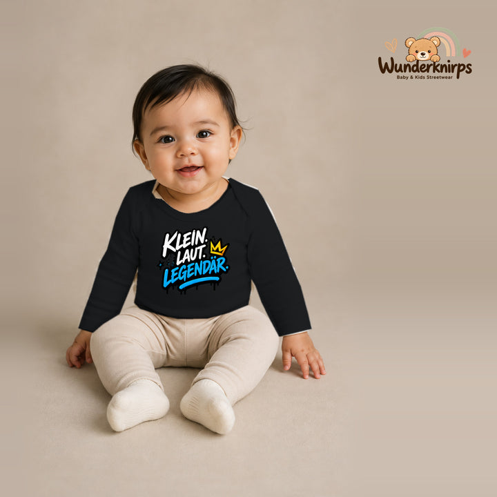 Babybody für Mädchen in Schwarz mit Motiv „Klein laut legendär“, getragen von einem Kind – Wunderknirps.