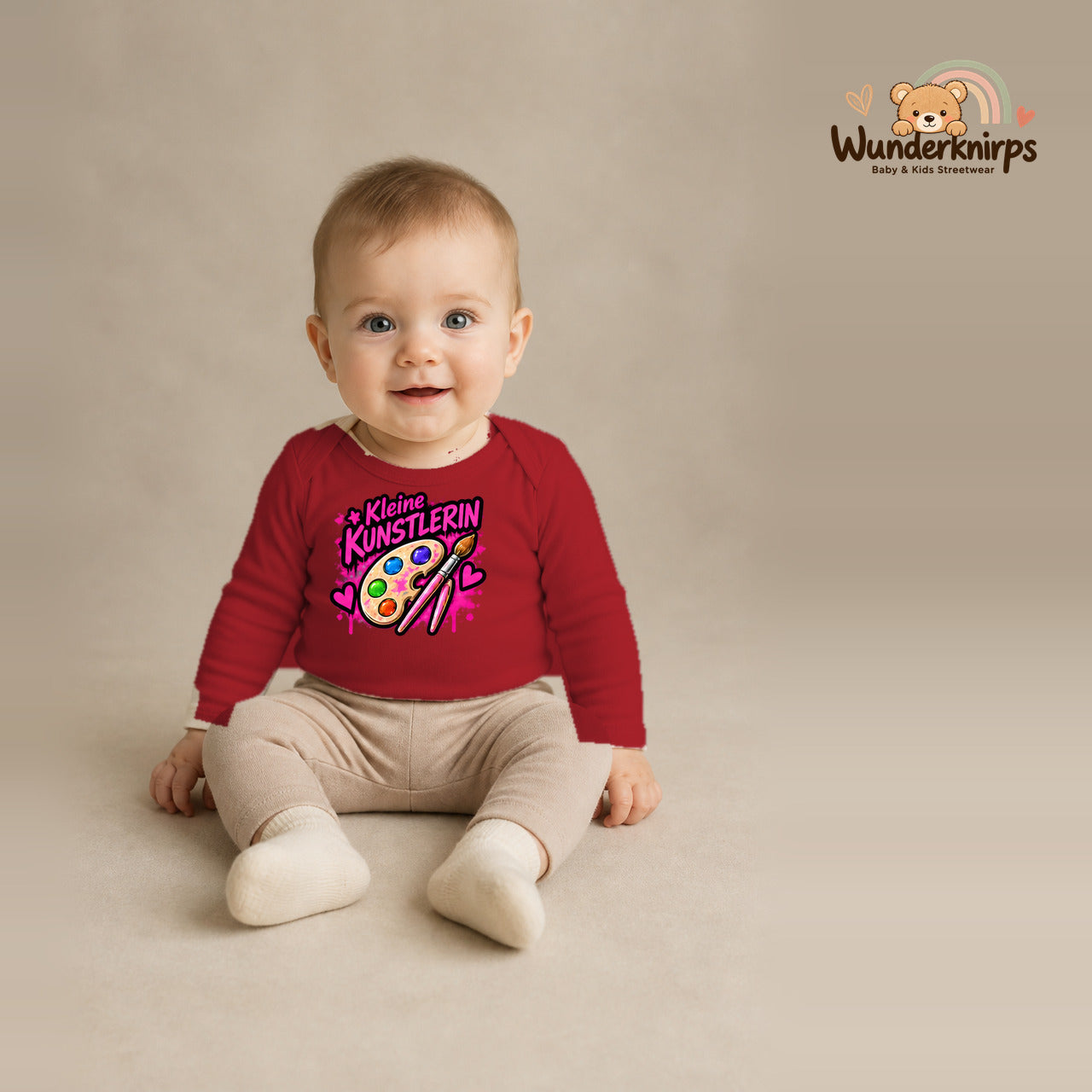 Babybody für Jungen in Rot mit Motiv „Kleine Künstlerin“, getragen von einem Kind – Wunderknirps.