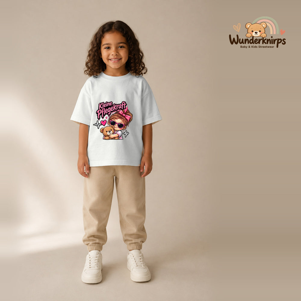 T-Shirt für Mädchen in Weiß mit Motiv „Kleine Pflegekraft“, getragen von einem Kind – Wunderknirps.