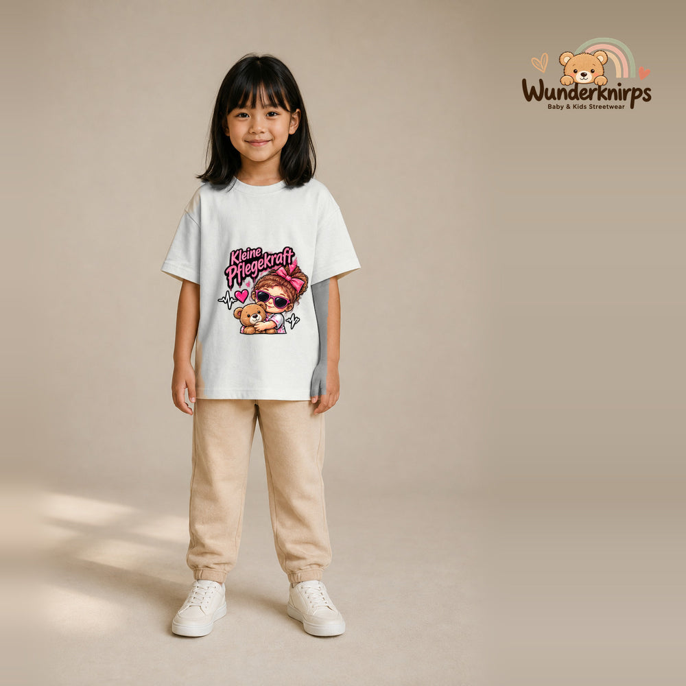 T-Shirt für Mädchen in Weiß mit Motiv „Kleine Pflegekraft“, getragen von einem Kind – Wunderknirps.