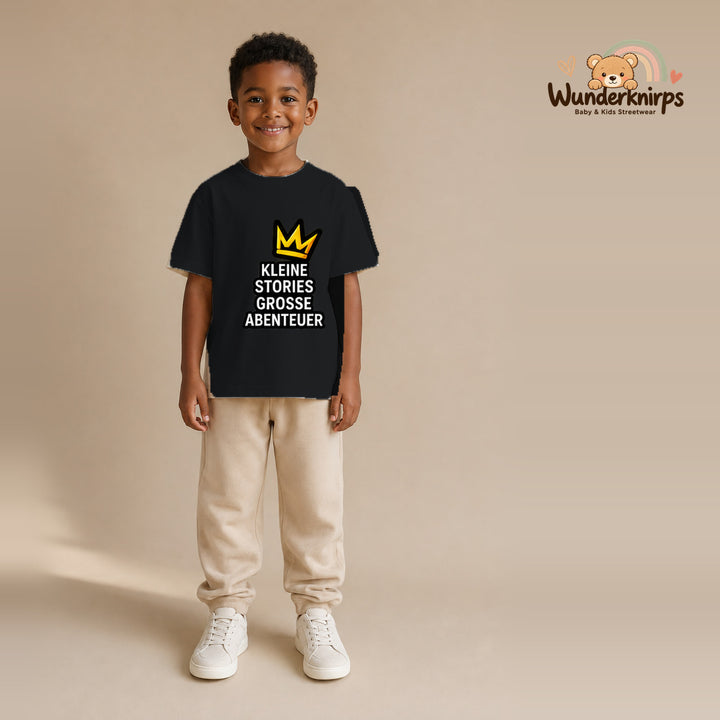 T-Shirt für Jungen in Schwarz mit Motiv „Kleine Stories große Abenteuer“, getragen von einem Kind – Wunderknirps.