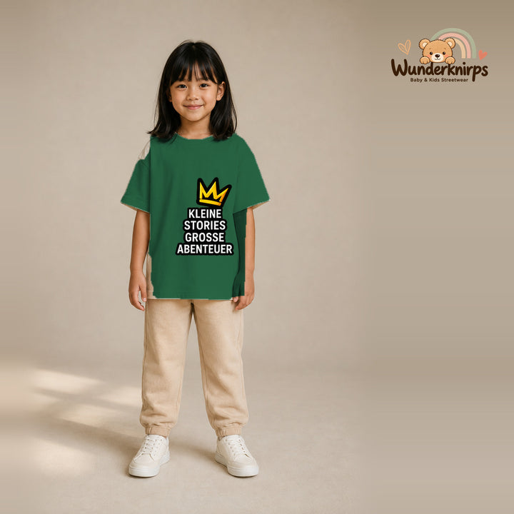 T-Shirt für Mädchen in Grün mit Motiv „Kleine Stories große Abenteuer“, getragen von einem Kind – Wunderknirps.