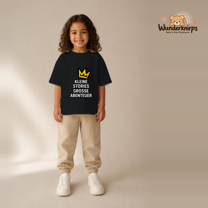 T-Shirt für Mädchen in Schwarz mit Motiv „Kleine Stories große Abenteuer“, getragen von einem Kind – Wunderknirps.