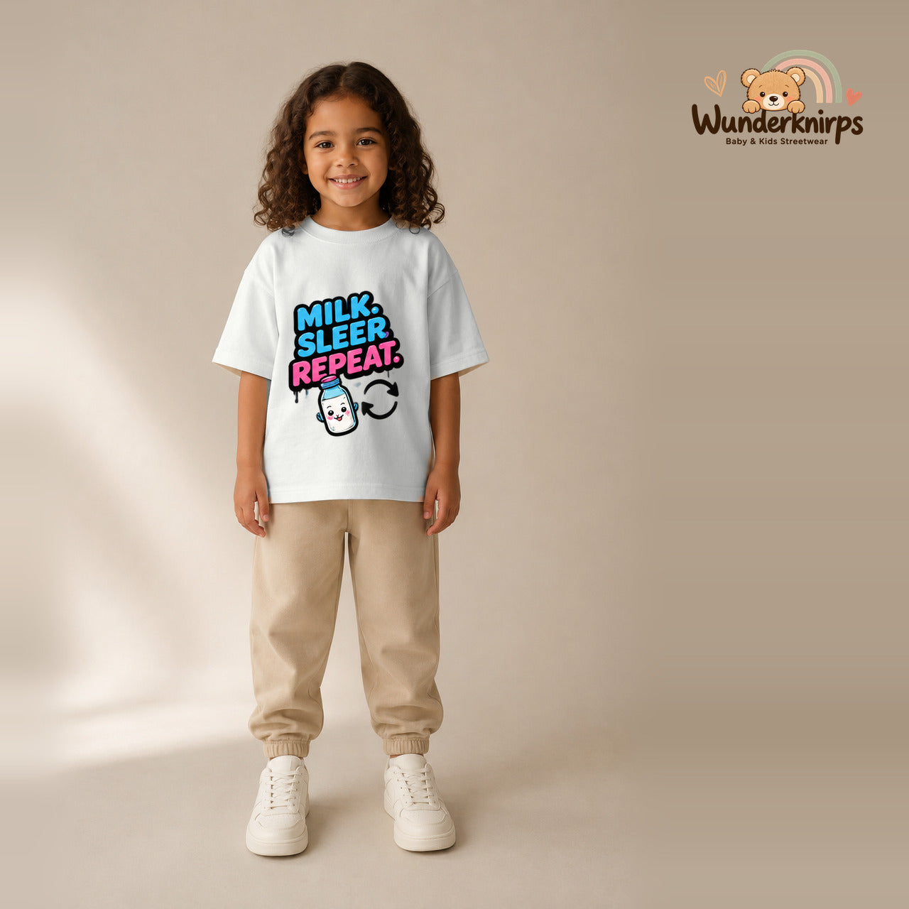T-Shirt für Mädchen in Weiß mit Motiv „Milk Sleep Repeat“, getragen von einem Kind – Wunderknirps.