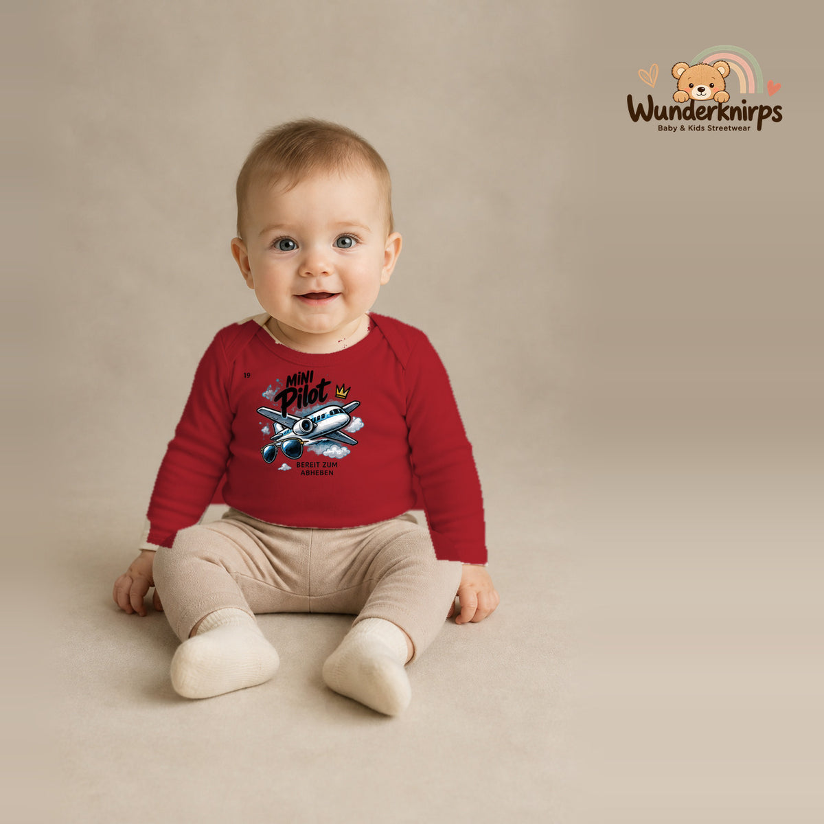 Babybody für Jungen in Rot mit Motiv „Mini Pilot“, getragen von einem Kind – Wunderknirps.