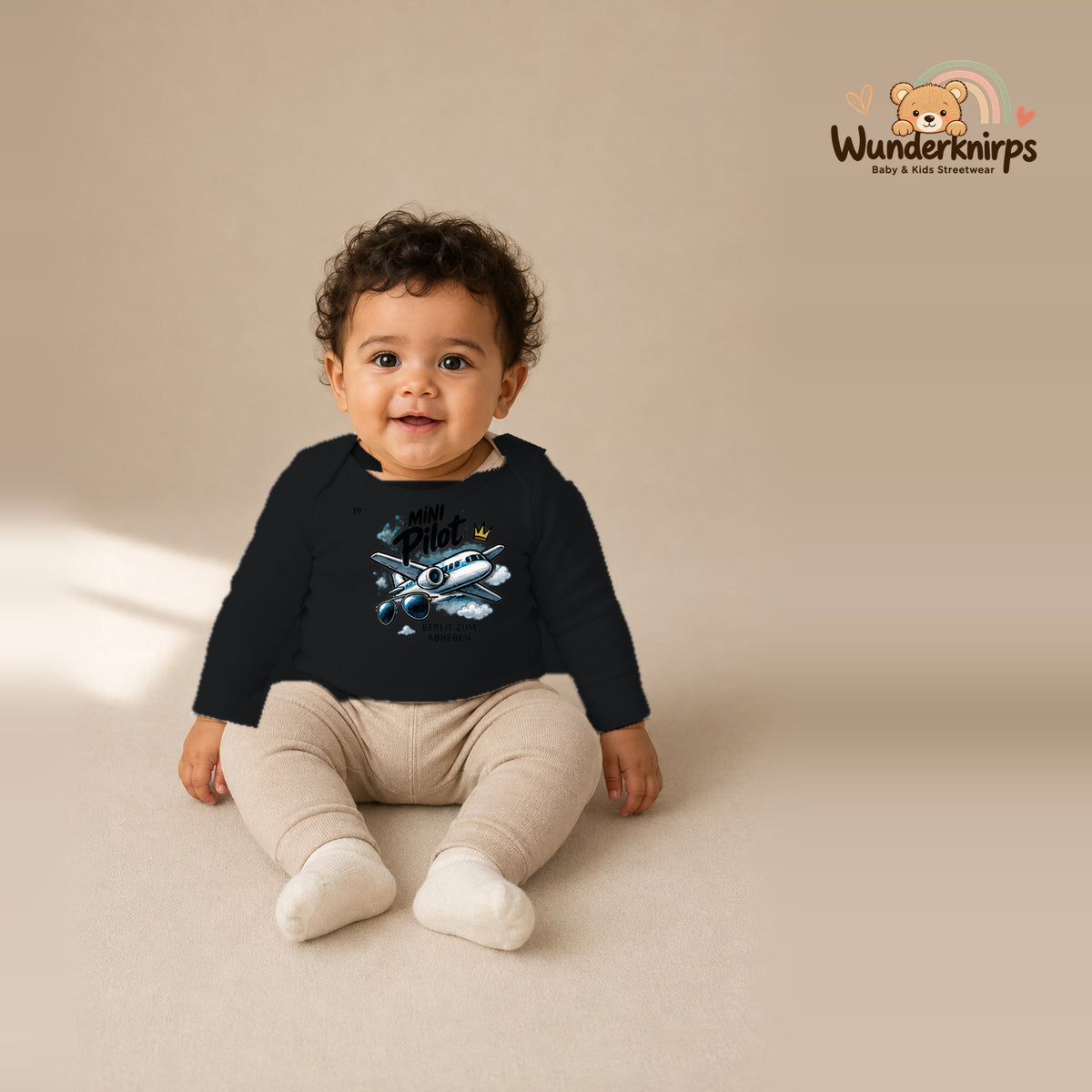 Babybody für Jungen in Schwarz mit Motiv „Mini Pilot“, getragen von einem Kind – Wunderknirps.