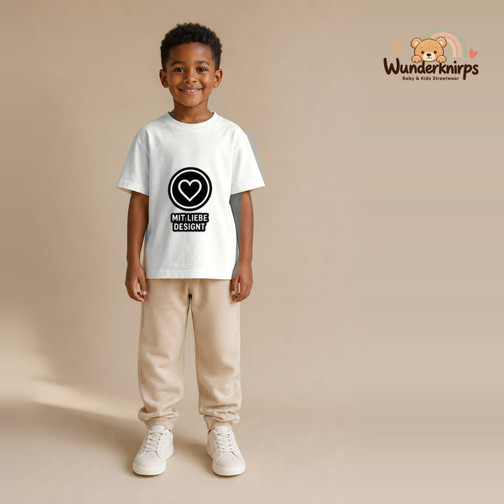 T-Shirt für Jungen in Weiß mit Motiv „Mit Liebe designt“, getragen von einem Kind – Wunderknirps.