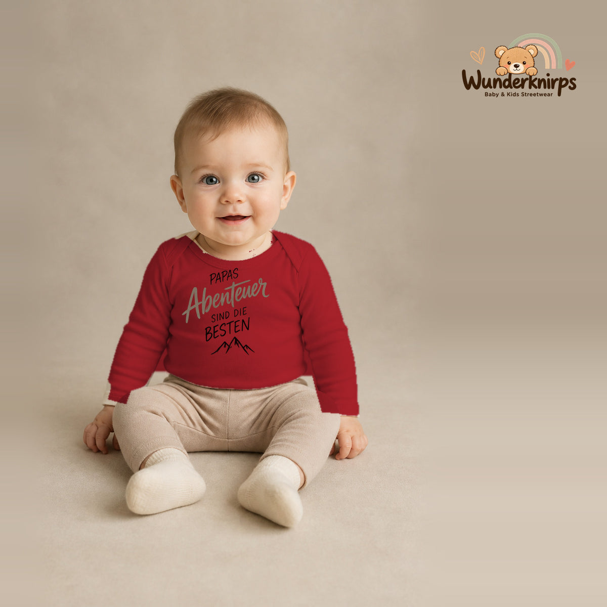 Babybody für Jungen in Rot mit Motiv „Papas Abenteuer“, getragen von einem Kind – Wunderknirps.