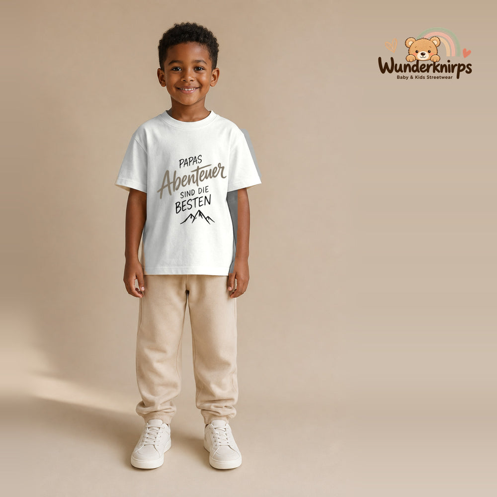 T-Shirt für Jungen in Weiß mit Motiv „Papas Abenteuer“, getragen von einem Kind – Wunderknirps.