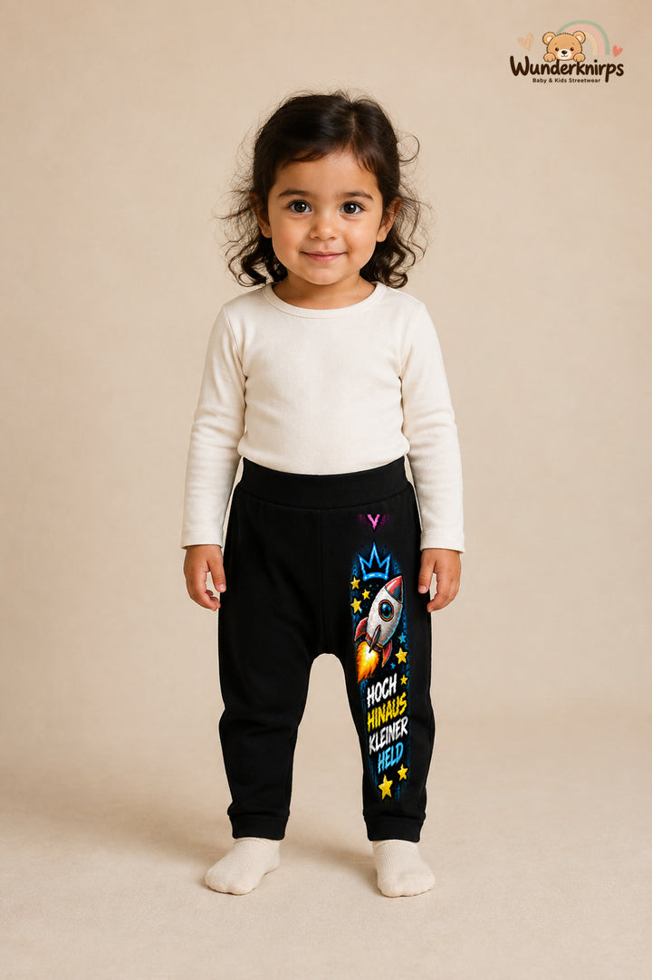 Rakete Traumlook – Hoch hinaus kleiner held – Babyhose für Mädchen: Schwarz mit Rakete-Druck am Hosenbein – Wunderknirps.