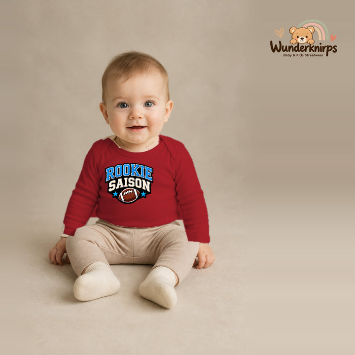 Babybody für Jungen in Rot mit Motiv „Rookie Saison“, getragen von einem Kind – Wunderknirps.