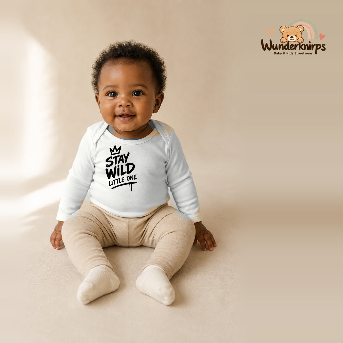 Babybody für Mädchen in Weiß mit Motiv „Stay Wild Little One“, getragen von einem Kind – Wunderknirps.