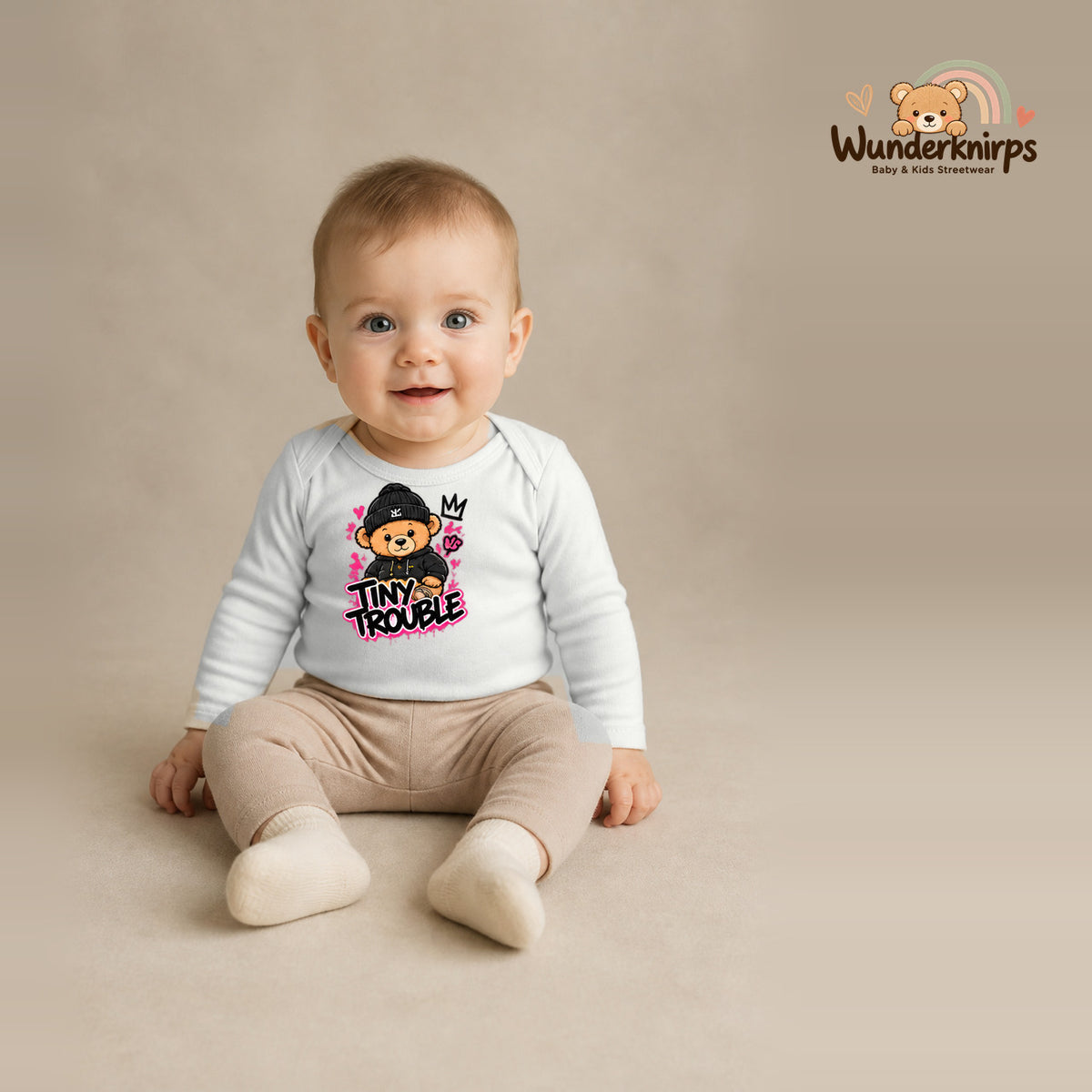Babybody für Jungen in Weiß mit Motiv „Tiny Trouble“, getragen von einem Kind – Wunderknirps.