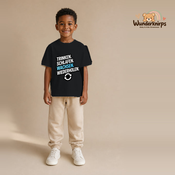 T-Shirt für Jungen in Schwarz mit Motiv „Trinken Schlafen Wachsen“, getragen von einem Kind – Wunderknirps.