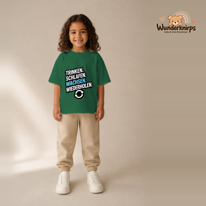 T-Shirt für Mädchen in Grün mit Motiv „Trinken Schlafen Wachsen“, getragen von einem Kind – Wunderknirps.