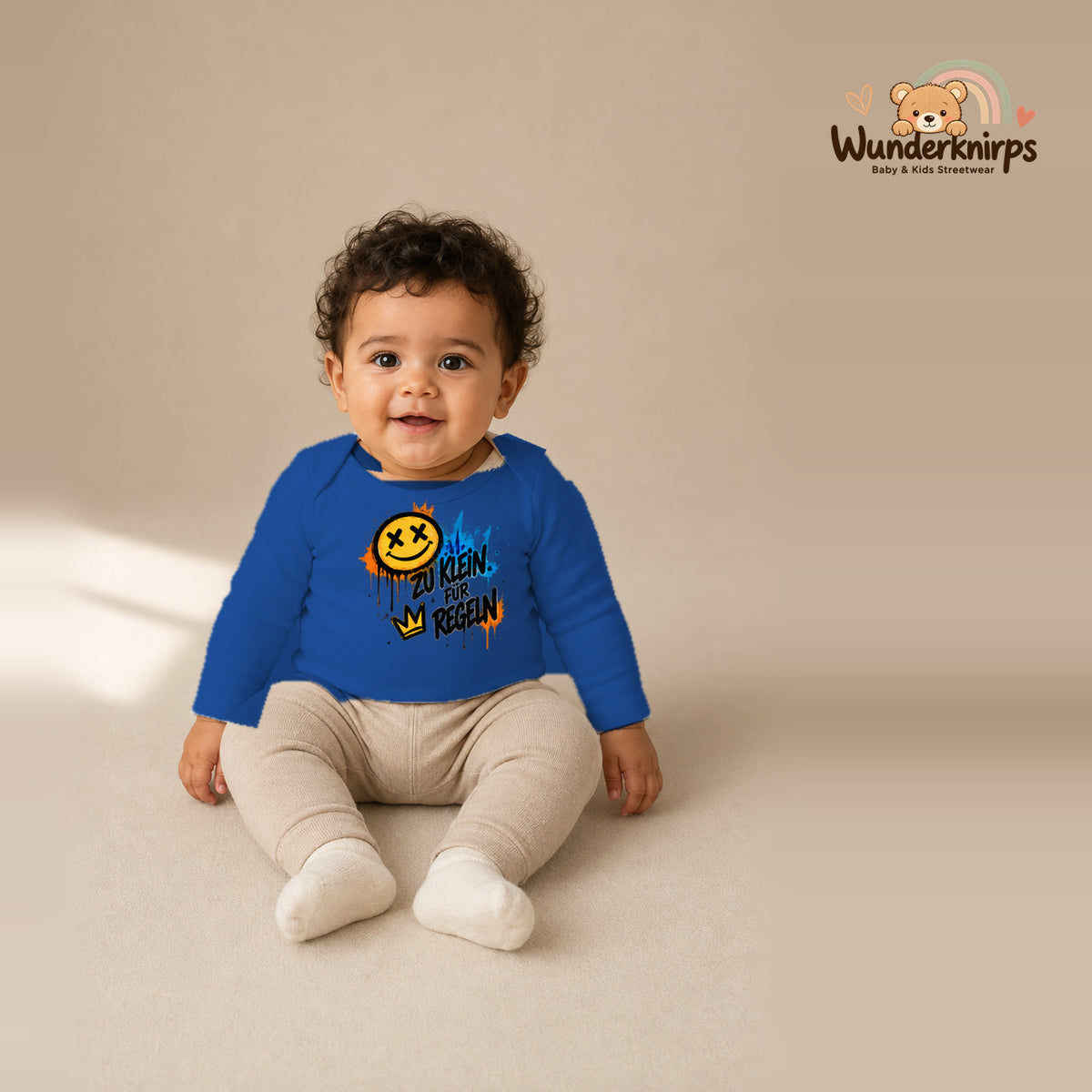 Babybody für Jungen in Blau mit Motiv „Zu klein für Regeln“, getragen von einem Kind – Wunderknirps.