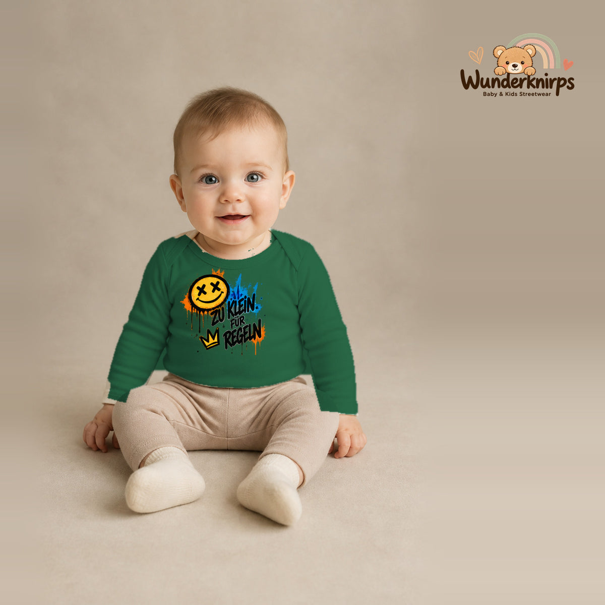 Babybody für Jungen in Grün mit Motiv „Zu klein für Regeln“, getragen von einem Kind – Wunderknirps.